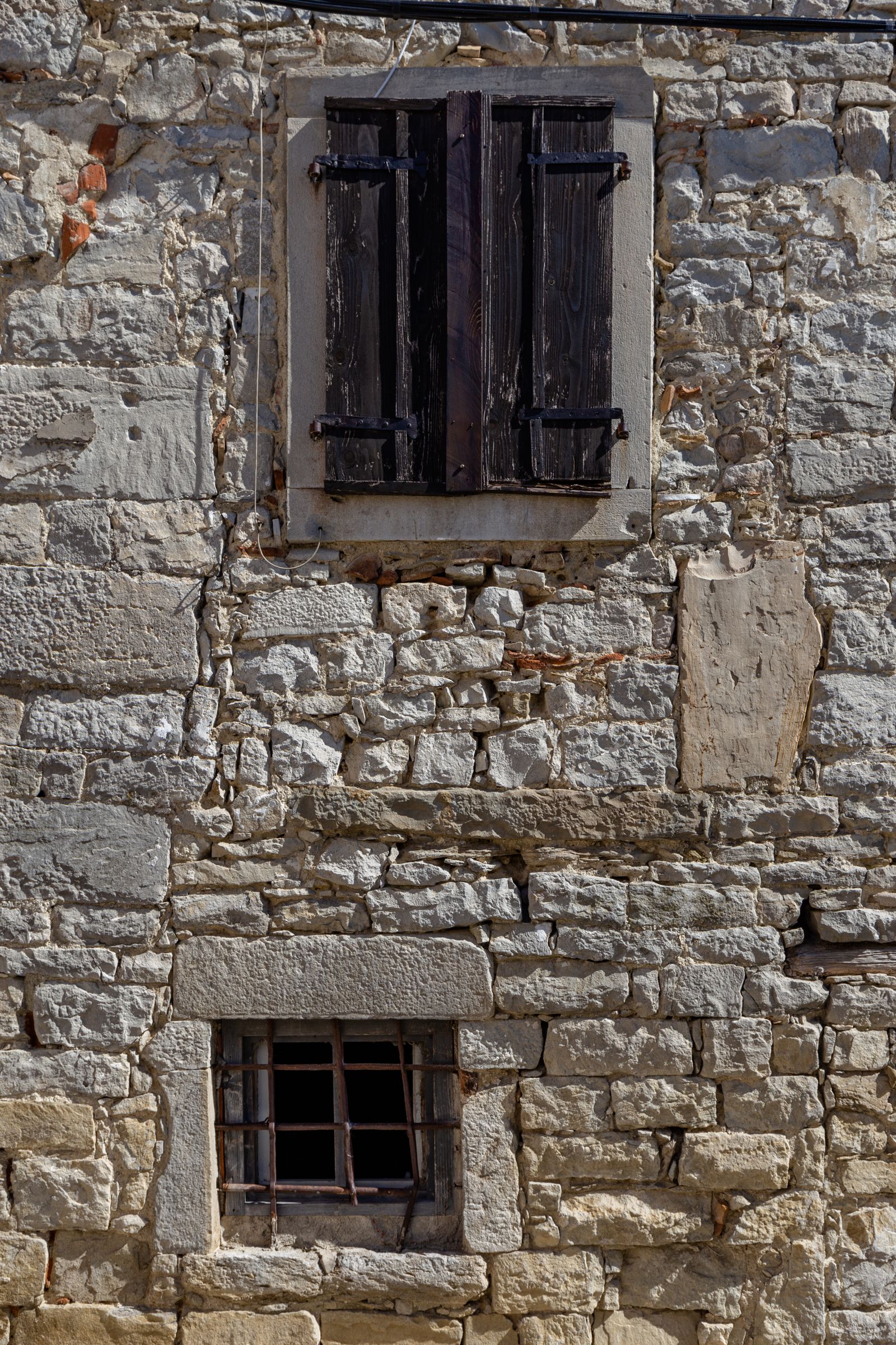 Weathered stone facade of an old house in Buzet with wooden shutters and a small barred window