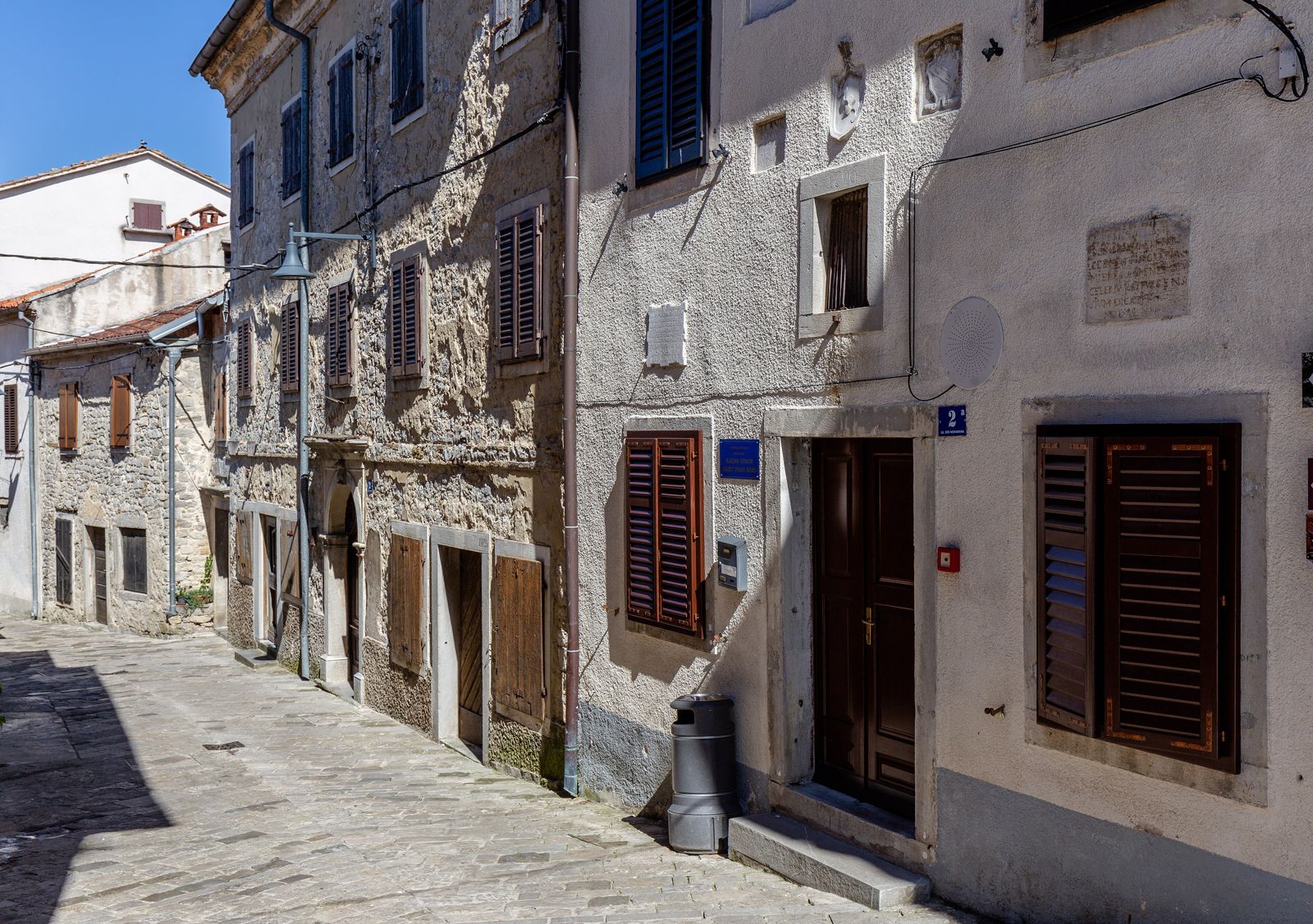 Street in Buzet with rendered house facades of different ages next to older stone buildings