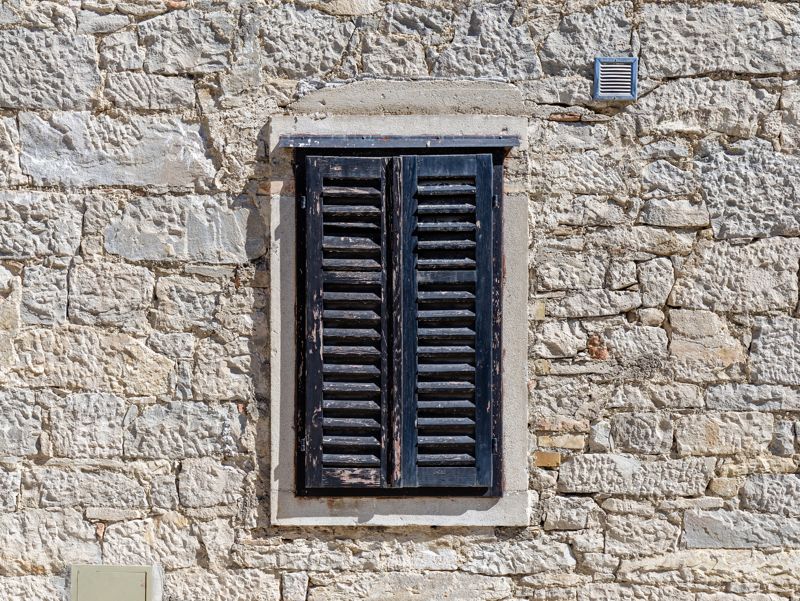 Old stone house window with closed wooden shutters in Buzet