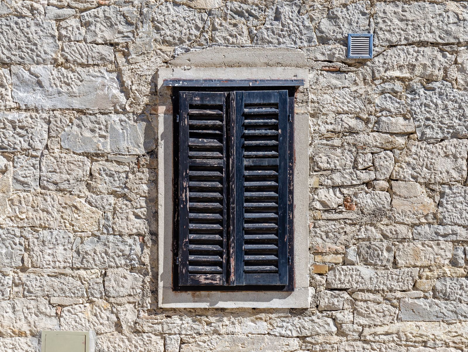 Small window with wooden shutters in an old stone wall in Buzet
