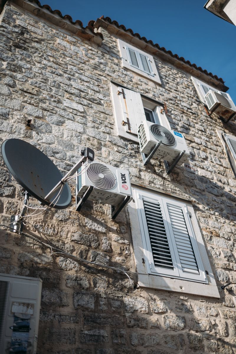 Stone house facade with several air conditioning units and a satellite dish
