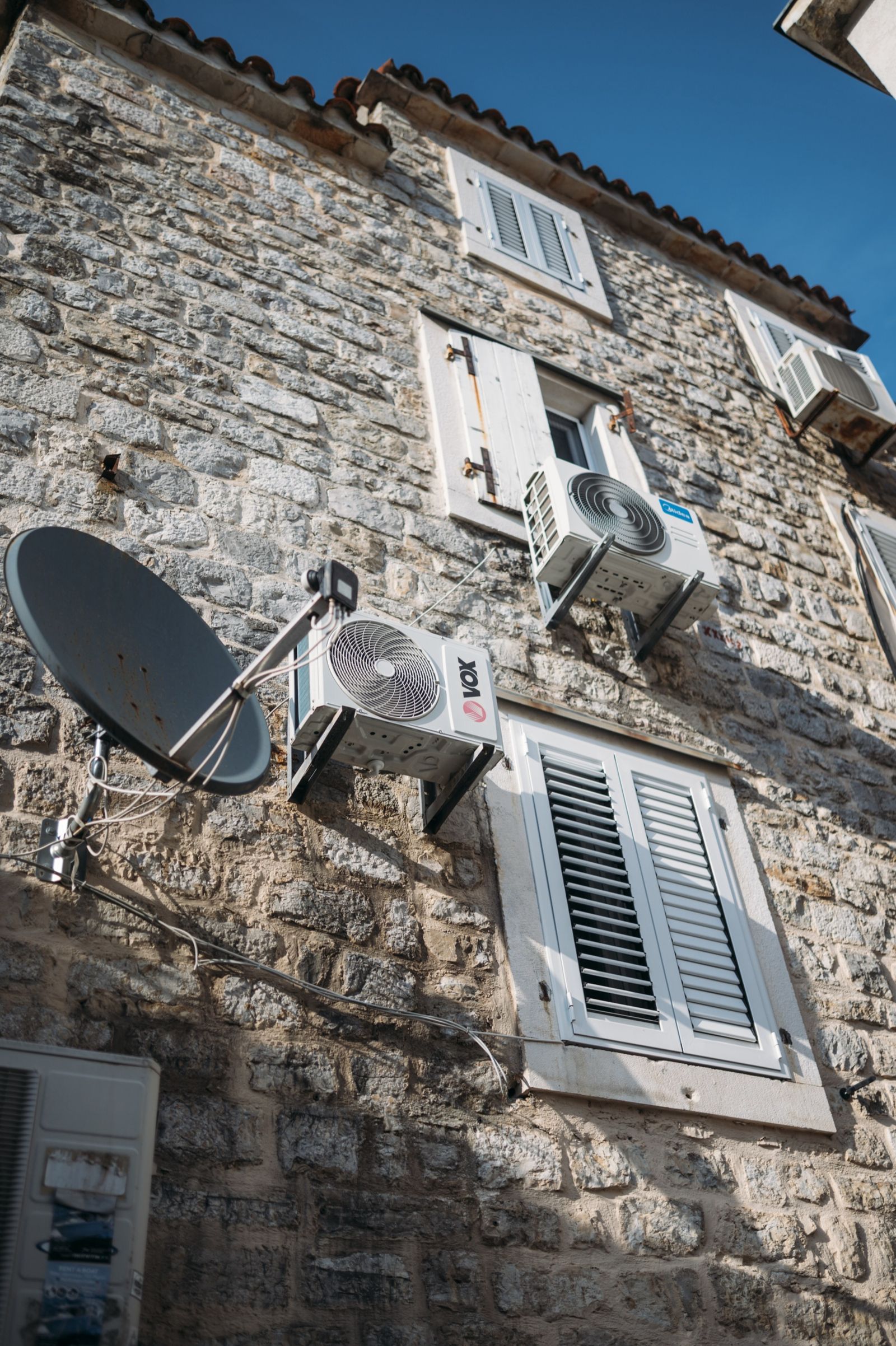 Stone house facade with several air conditioning units and a satellite dish