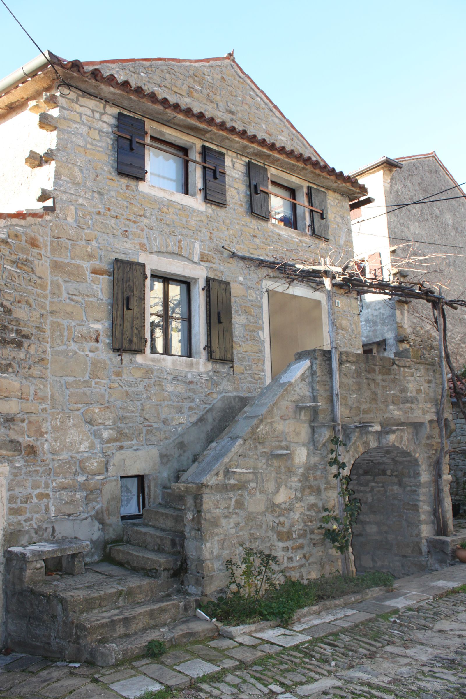 Two-storey Istrian stone house with wooden shutters and an external stone staircase (baladur) on a cobbled street