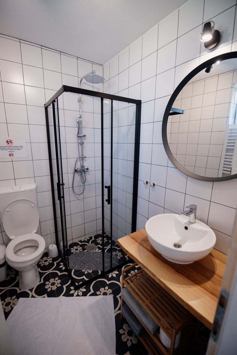 Small modern bathroom with a glass corner shower, round mirror and compact vanity