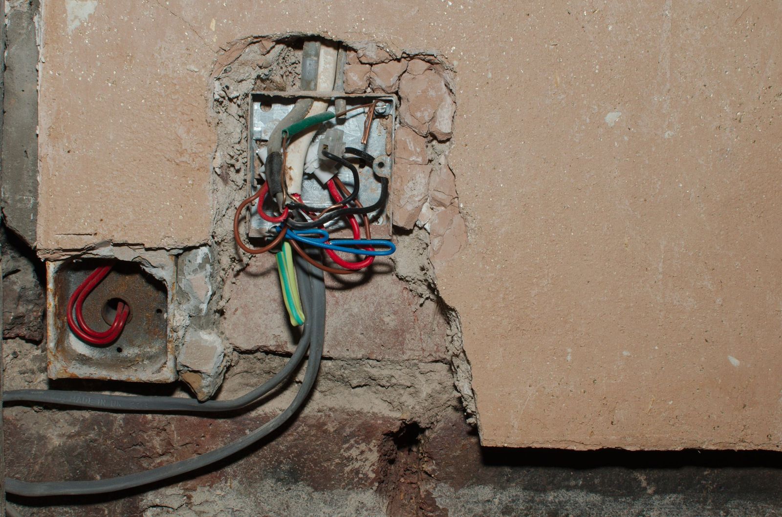 Old wiring and a junction box exposed in an opened plaster wall