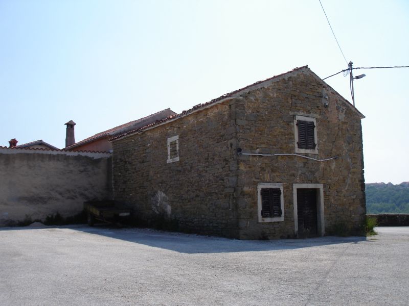 Old two-storey limestone house with small windows and a clay tile roof in the village of Momjan