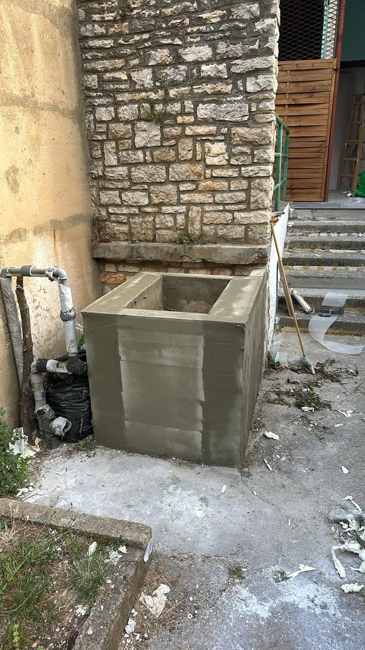 Courtyard repair at the base of an old stone wall, with new blockwork and pipes being rerouted