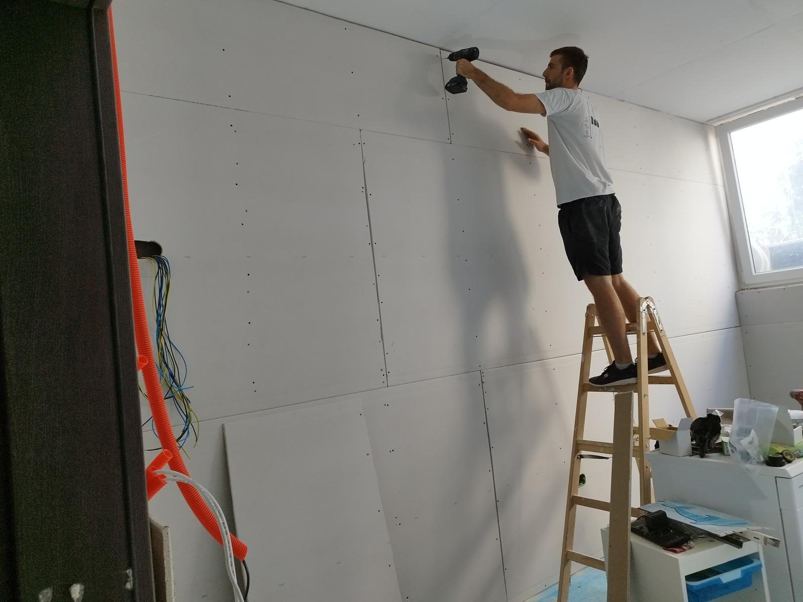 Drywall ceiling being fixed to a metal frame in a room under renovation